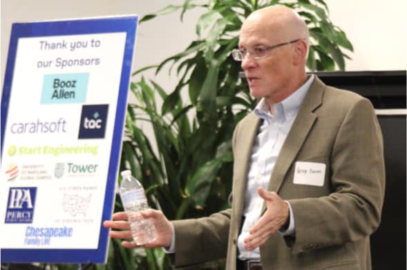 convening to act education summit speaker on stage with sponsor sign in background convening to act education summit speaker on stage with sponsor sign in background