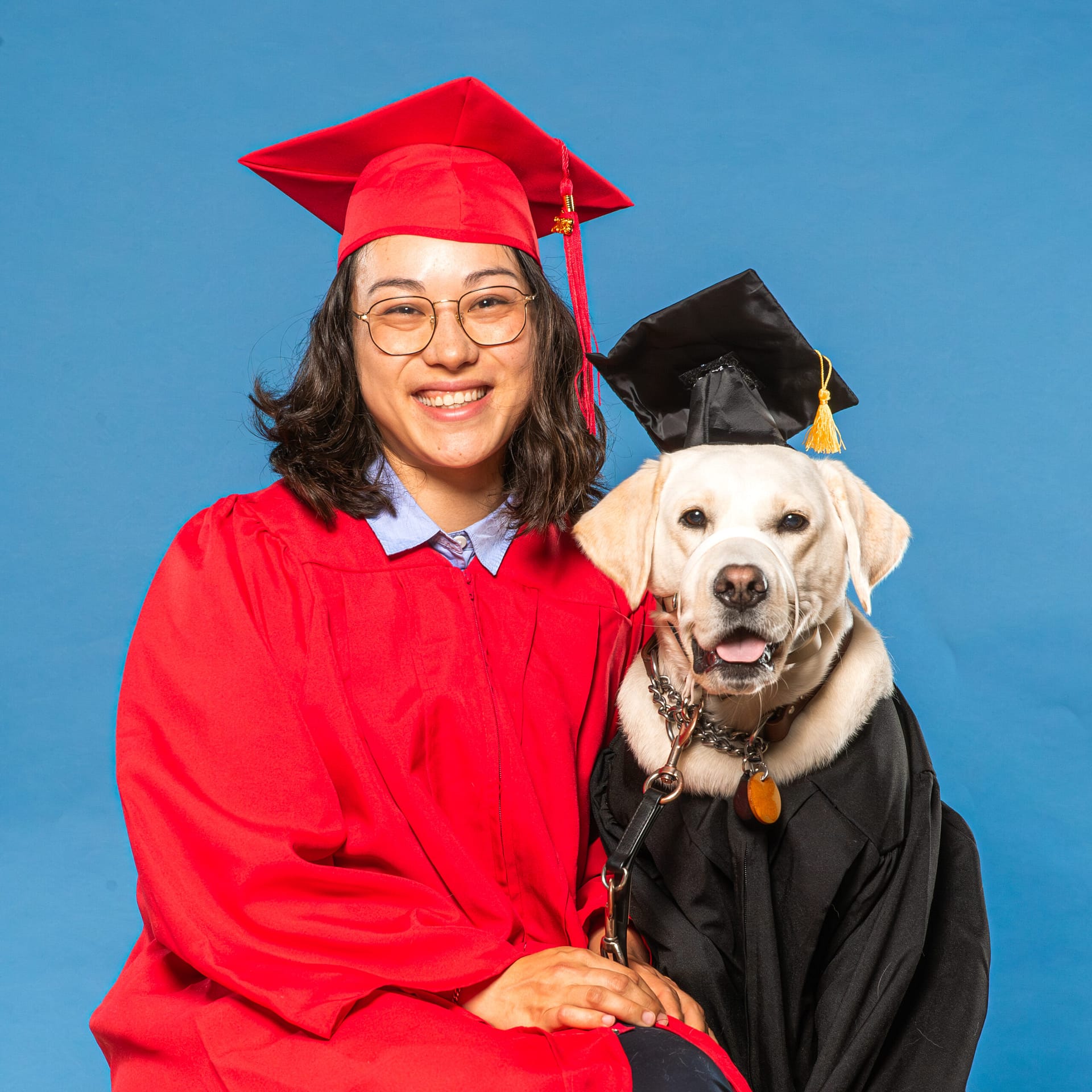 women in graduation gown sits next to dog in graduation gown